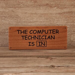 May include: A wooden sign with the text "The Computer Technician is IN" in black lettering.