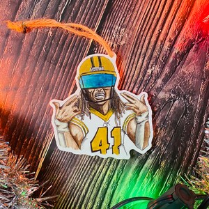 May include: A watercolor illustration of a football player wearing a yellow helmet with a blue face mask. The player is wearing a white jersey with gold trim and the number 41. The jersey has the word "Saints" on the front. The player is making a hand gesture with both hands.