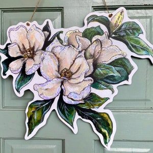 May include: A white paper cut-out of a magnolia flower bouquet with green leaves. The flowers have a pearlescent finish.