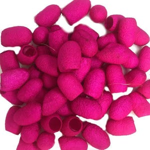 May include: A collection of numerous small, oval-shaped silkworm cocoons dyed in a vibrant hot pink colour. Each individual cocoon features a textured, fibrous surface and a single circular opening at one end, scattered together in a dense pile.