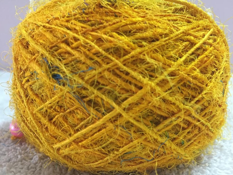 May include: A ball of yellow yarn with blue and green accents. The yarn is made of natural fibers and has a rustic, hand-spun look.