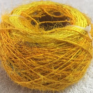 May include: A skein of yellow and gold silk yarn, wound into a ball shape. The yarn is soft and fluffy, with a slightly textured surface.