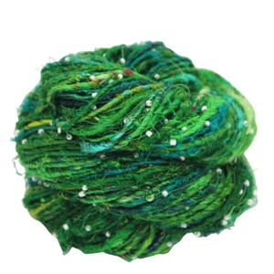 May include: A skein of green silk yarn with white beads woven throughout. The yarn is a mix of shades of green, including emerald, forest, and teal.