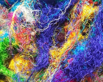May include: A dense, tangled pile of multi-colored sari silk yarn fibers. The collection features vibrant, saturated hues including royal blue, emerald green, bright yellow, magenta, and purple, with thin, metallic gold threads woven throughout.