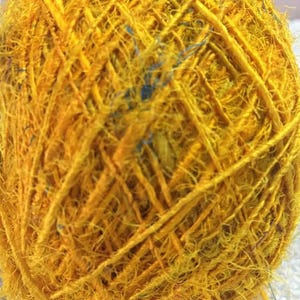 May include: A ball of yellow yarn with a few blue strands woven in. The yarn is very fuzzy and has a rustic look.