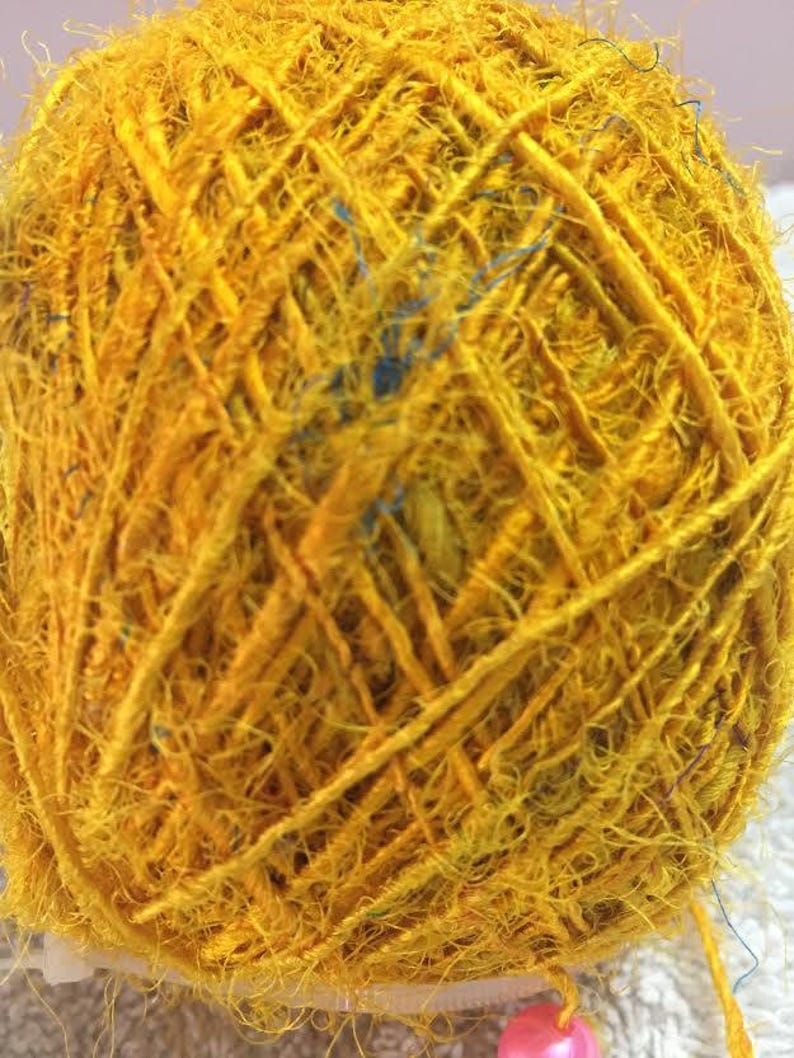 May include: A ball of yellow yarn with a few blue strands woven in. The yarn is very fuzzy and has a rustic look.