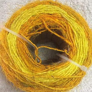 May include: A skein of yellow and orange yarn, tied with a white plastic tie. The yarn is made of natural fibers and has a fuzzy texture.