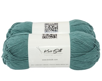 May include: Two teal-colored yarn skeins. Each skein is wrapped with a white label featuring the text "Knit Silk" and a QR code. The yarn is tightly wound, showing a textured surface, ideal for knitting, crochet, and other crafts.