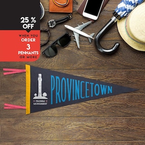 Op de afbeelding: Een marineblauwe wimpel met het woord "PROVINCETOWN" in blauwe letters. De wimpel toont een illustratie van een toren en de tekst "PILGRIM MONUMENT". De afbeelding bevat ook reisaccessoires en een kortingsaanbieding.