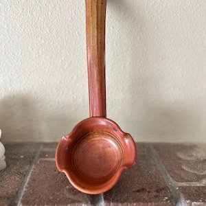 May include: A ceramic ladle with a long, textured handle and a round, bowl-shaped head. The piece features a warm, earthy terracotta glaze with subtle variations in color, including hints of yellow and brown throughout the surface.