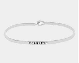 May include: A silver bangle bracelet with a simple design and the word "FEARLESS" engraved on the front.