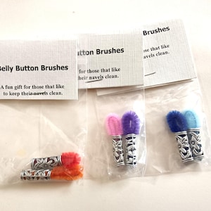 May include: Three sets of belly button brushes in clear plastic bags. Each brush has a decorative silver-coloured handle and a fluffy, colourful brush head. The packaging reads "Belly Button Brushes" and "A fun gift for those that like to keep their navels clean."