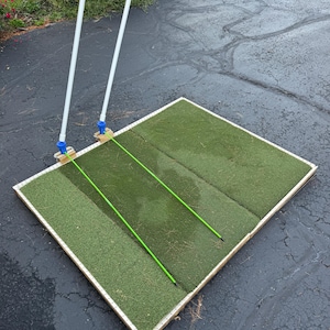 May include: A green artificial turf putting green with two white poles and green lines. The putting green is on a wooden frame.