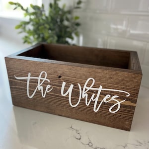 May include: A brown wooden box with the words "The Whites" written in white paint on the front.