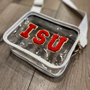 Op de afbeelding: Transparante plastic crossbody tas met een witte rand en een rood en gouden "ISU" patch.