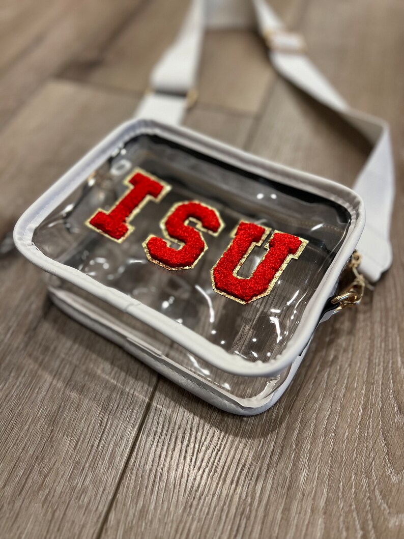 Op de afbeelding: Transparante plastic crossbody tas met een witte rand en een rood en gouden "ISU" patch.