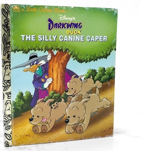 May include: A Little Golden Book featuring Disney's Darkwing Duck. The cover shows Darkwing Duck hiding behind a tree, while four brown and white puppies run through the grass. The title of the book is "The Silly Canine Caper."