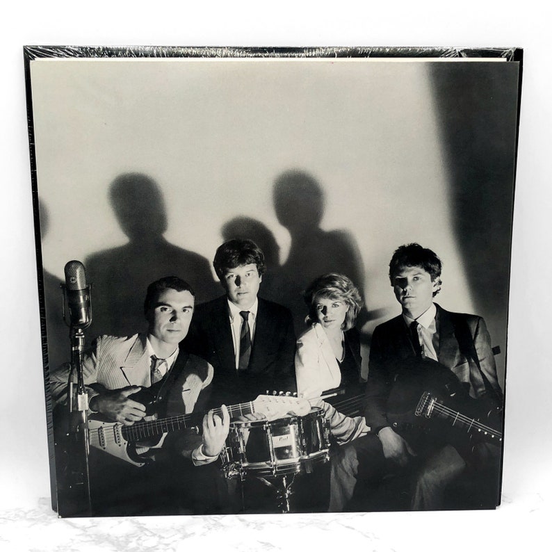 Puede incluir: Foto en blanco y negro de una banda con cuatro miembros. Los miembros de la banda est&aacute;n sentados frente a un micr&oacute;fono y una bater&iacute;a. Los miembros de la banda sostienen guitarras y un micr&oacute;fono.