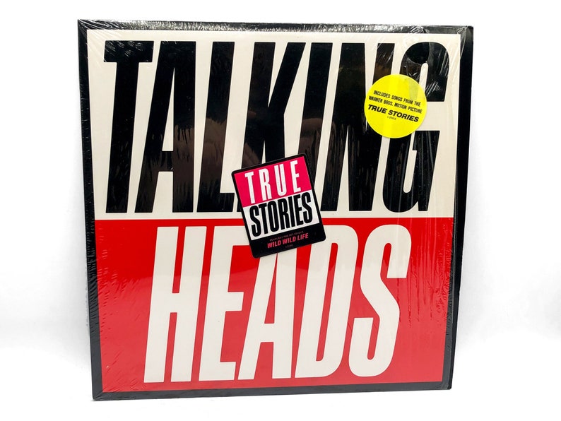 Puede incluir: Una portada de disco de vinilo en blanco y negro con las palabras "Talking Heads" en letras blancas grandes y en negrita. El t&iacute;tulo del &aacute;lbum "True Stories" est&aacute; en una fuente m&aacute;s peque&ntilde;a, rosa con un borde negro. La portada es roja y blanca con una pegatina amarilla que dice "Includes songs from the Warner Bros. motion picture True Stories."
