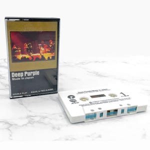 May include: A white cassette tape with the text "Deep Purple/Made in Japan" printed on the front. The cassette tape is a double play, equal to two albums. The cassette tape is in a plastic case with a black and gold design. The case has the text "Deep Purple Made in Japan" printed on the front.