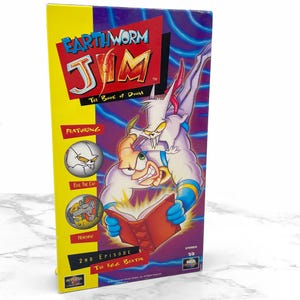 May include: A VHS tape featuring the cartoon Earthworm Jim. The cover features a purple background with a blue and white character, Earthworm Jim, holding a red book. The text on the cover reads "Earthworm Jim: The Book of Doom".