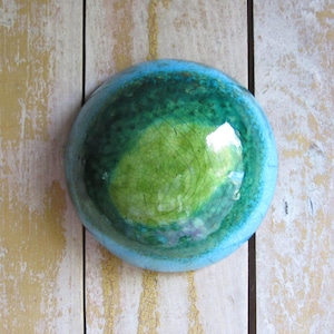 May include: A round ceramic bowl featuring a glossy glaze with a gradient of colors transitioning from a bright lime green center to a deep forest green middle and a light sky blue rim, all finished with a fine crackle texture.