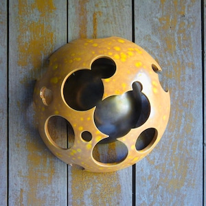 May include: A round, ceramic wall sculpture with a yellow glaze and multiple cut-out circles. The sculpture has a textured surface and a slightly raised center.