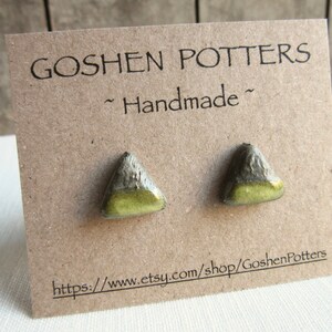 May include: A pair of triangular ceramic earrings with a green glaze and a brown speckled finish. The earrings are displayed on a card that reads "Goshen Potters ~ Handmade ~" and includes a website address.