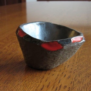 May include: A small, black ceramic bowl with a textured surface and a red rim.