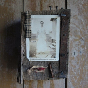 May include: A rustic wooden frame with a black and white photo of a man in a white shirt and pants. The frame is decorated with fabric scraps and nails. The text "I have work to do and courage to perform it." is printed on the frame.