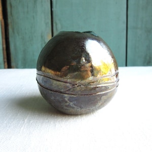May include: A round, metallic, ceramic vase with a dark brown and gold glaze. The vase has a smooth, shiny surface and a slightly indented opening at the top.