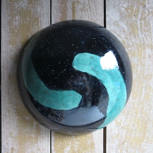 May include: A black ceramic bowl with a teal glaze and a swirling design. The bowl has a glossy finish and is speckled with small white dots.