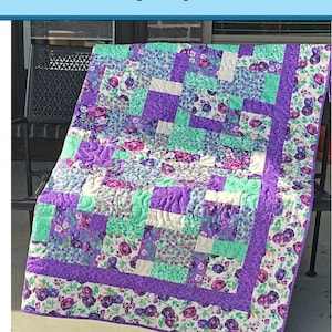 May include: A quilt pattern for a charm square quilt called "Charming Four Patch". The quilt is made with purple, white, and green floral fabric. The finished size of the quilt is 58 inches by 65 inches.