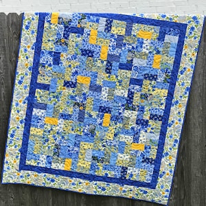 May include: A blue and yellow patchwork quilt with a floral print. The quilt is edged with a blue border and a floral trim.
