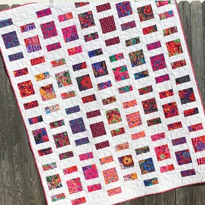 May include: A white quilt with a grid pattern of colourful squares. The squares are filled with various floral and geometric designs in shades of pink, red, purple, and blue.