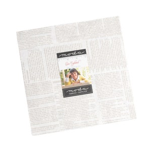 May include: A white fabric with a newspaper print design. The fabric features a black and white label with the text "moda fabrics + supplies" and a photo of a woman. The label also includes the text "Ann  Eckelkamp  Fig Tree & Co."