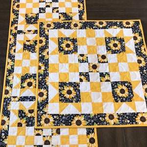 Pode incluir: Dois corredores de mesa acolchoados amarelos e brancos com uma borda floral preta e branca. O corredor de mesa menor está em cima do maior.