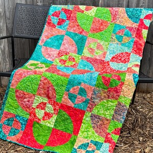 May include: A colorful quilt with a geometric pattern of circles and squares in shades of green, red, and blue. The quilt is made of fabric with a floral print.
