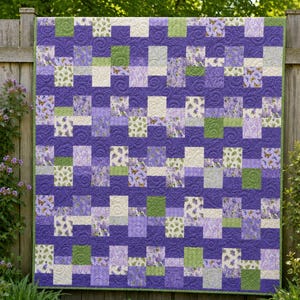 May include: A patchwork quilt featuring a repeating grid of square fabric blocks in shades of deep purple, light lavender, sage green, and cream. The design incorporates solid purple blocks with a swirling texture and patterned blocks with butterflies.