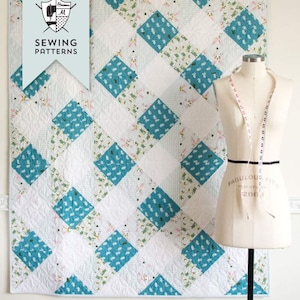 May include: A quilt pattern for a Gingham Daydream Quilt. The quilt is made with a white background and blue and green patterned squares. The pattern includes instructions for both lap and twin sized quilts.
