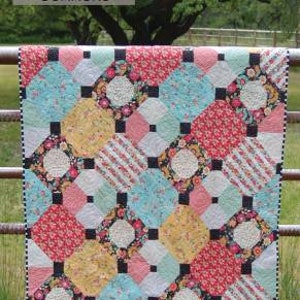 May include: A quilt pattern called "Just Smashing #205" from Cotton Street Commons. The quilt is made with a variety of colorful fabrics in a geometric pattern. The quilt is hanging on a wooden fence.