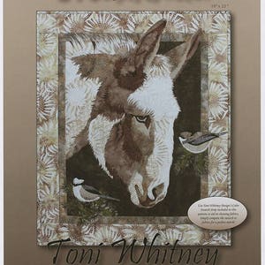 May include: A quilt pattern featuring a close-up of a donkey's head with a white and brown coat. The donkey is framed by a floral pattern and two small birds are perched on branches. The title "Matilda" is written in cursive at the top of the image. The text "Toni Whitney design" is at the bottom of the image. The quilt pattern is 19 inches by 23 inches.