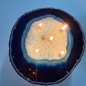 May include: A lit candle set in a large, round, blue and white agate stone. The candle flames are bright against the stone's natural patterns. The agate has a dark blue outer edge, transitioning to lighter blue and white in the centre.