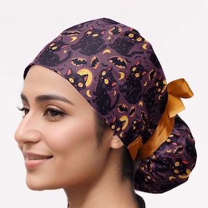 May include: A purple scrub cap featuring a repeating pattern of black cats with yellow eyes, yellow crescent moons, and small bats. The cap includes a gathered back section secured with a solid mustard yellow ribbon tied into a bow.