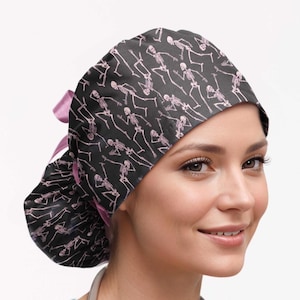 May include: A black scrub cap featuring a repeating pattern of light pink skeletons in various poses. The cap has a rounded crown, a gathered back section, and a light pink ribbon tie closure at the nape of the neck to secure the fit.