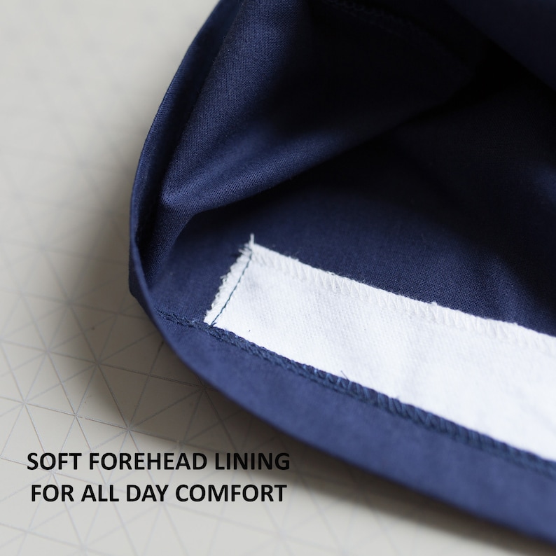 K&ouml;nnte beinhalten: Nahaufnahme des Innenraums eines marineblauen Hutes, der eine wei&szlig;e Stoffauskleidung zeigt. Der Text "SOFT FOREHEAD LINING FOR ALL DAY COMFORT" ist unter dem Hut aufgedruckt.
