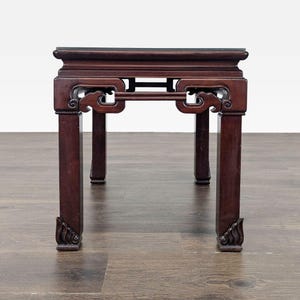 May include: A dark brown wooden side table featuring a flat square top, four straight legs, and decorative carved apron detailing under the tabletop. The base of each leg displays a carved flame-like motif, showcasing a polished wood finish.