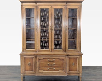 Könnte beinhalten: Ein hoher Vitrinenschrank aus Holz mit vier verglasten Türen im oberen Bereich, wobei die beiden mittleren Türen ein Rautenmuster aufweisen. Der Unterbau besteht aus drei mittigen Schubladen und zwei Seitenschränken, alle mit Messingbeschlägen.