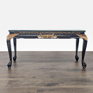 May include: A black rectangular console table with a glass top, featuring gold-painted carved details along the apron and cabriole legs that terminate in claw-and-ball feet. The frame displays intricate geometric fretwork and ornate accents.