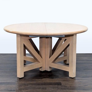 May include: A round wooden dining table with a light finish. The table has a solid base with angled supports and a two-piece tabletop. The table is approximately 48 inches in diameter.